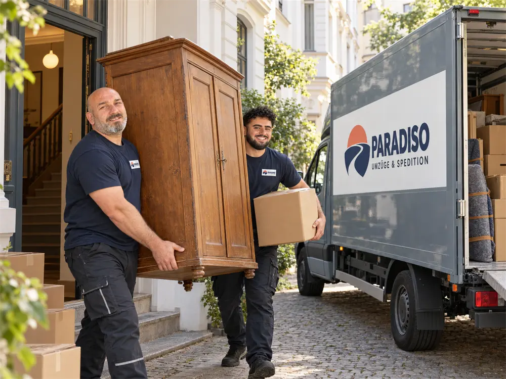 Zwei Umzugshelfer tragen einen alten Holzschrank aus einem Altbau zum LKW